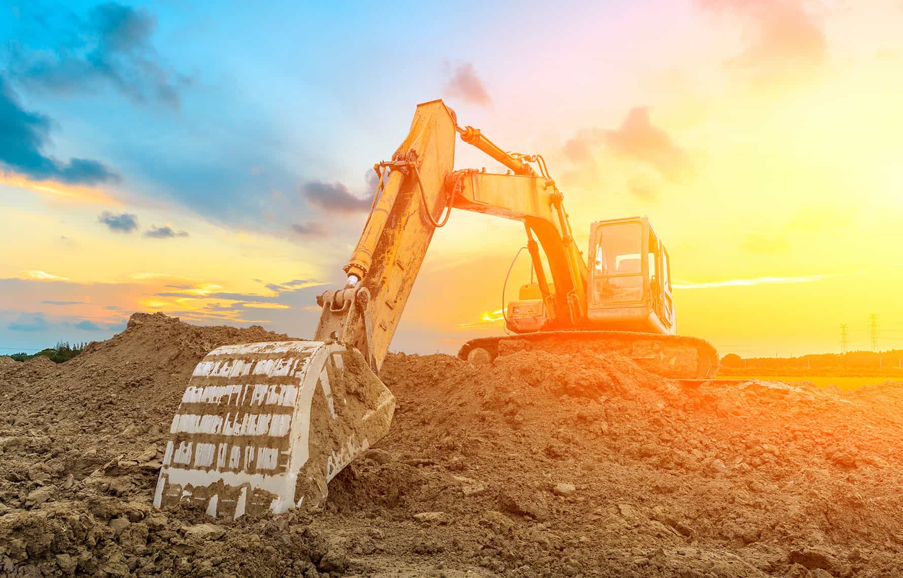 Heavy equipment with a scoop arm moving dirt, surrounded by the glow of the yellow and orange setting sun